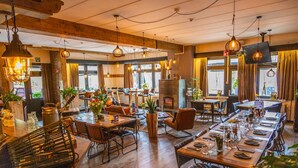A restaurant with wooden tables and chairs, hanging lights, and large windows. - Chalet With air Conditioning 16 km From Maastricht (Zutendaal)