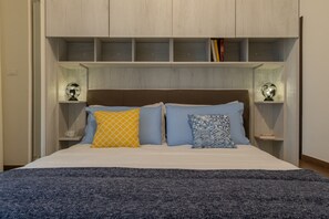 Una camera da letto con un letto, due comodini, una testiera e scaffali a parete sopra il letto.