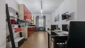 A modern kitchen with red and white cabinetry, a black countertop, and a dining area with a table set for two. - Turin World Apartment by Wonderful Italy (Turin)