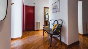 A hallway with wooden flooring, a red door, a black metal bench with a cushion, and a framed picture on the wall. - Classic Apartment La Maddalena by Wonderful Italy (Catania)
