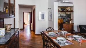 A dining area with a wooden table set for four, flanked by chairs, and a kitchen area with cabinets and appliances. - Classic Apartment La Maddalena by Wonderful Italy (Catania)