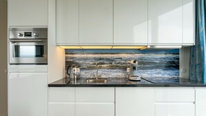 A modern kitchen with white cabinets, a stainless steel oven, a coffee maker, and a sink. - Beautiful Apartment With sea View (Scherpenisse)