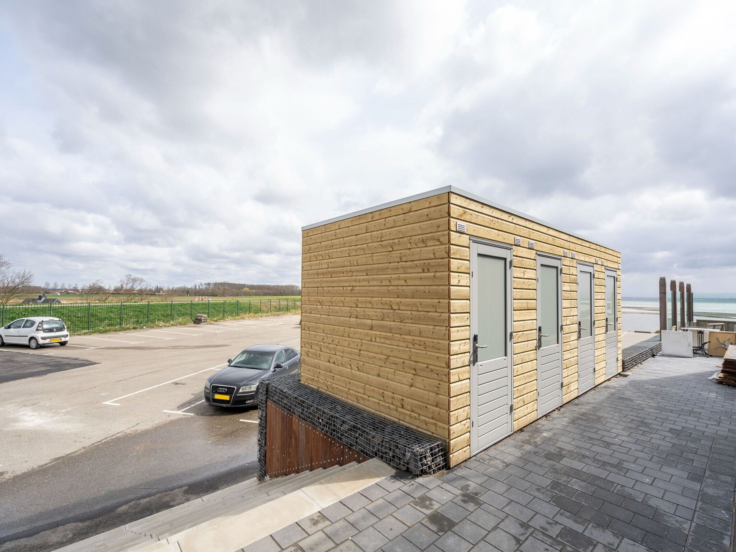 A small wooden building with two doors, adjacent to a paved area with parked cars.