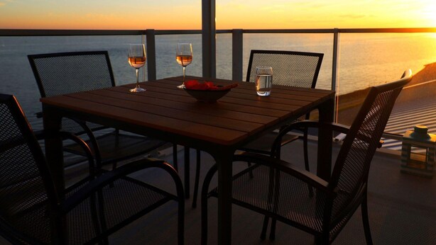 A table with two glasses of wine and a bowl, set on a balcony overlooking the sea at sunset. - Beautiful Apartment With sea View (Scherpenisse)