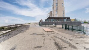 A modern building with a cylindrical tower, a paved walkway, and a rocky shoreline. - Beautiful Apartment With sea View (Scherpenisse)