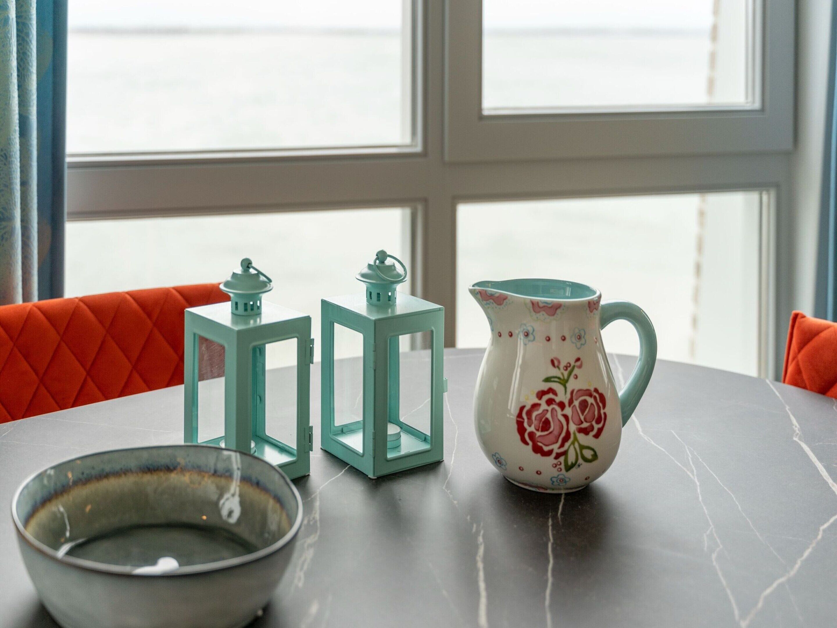 Uma mesa com uma tigela, duas lanternas azul-turquesa e um jarro floral.