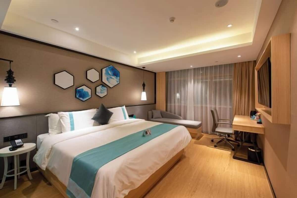 A hotel room with a large bed, a desk, a chair, and a TV.