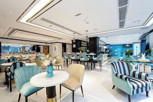 A modern hotel lobby with seating areas, a bar, and a view of the city.