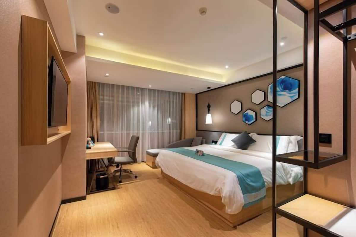 A modern hotel room with a large bed, a desk with a chair, and a TV mounted on the wall.