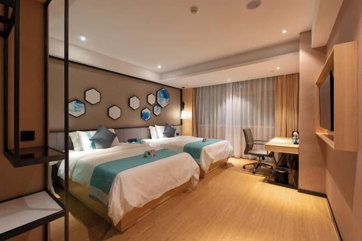 A hotel room with two beds, a desk, a chair, and a TV.