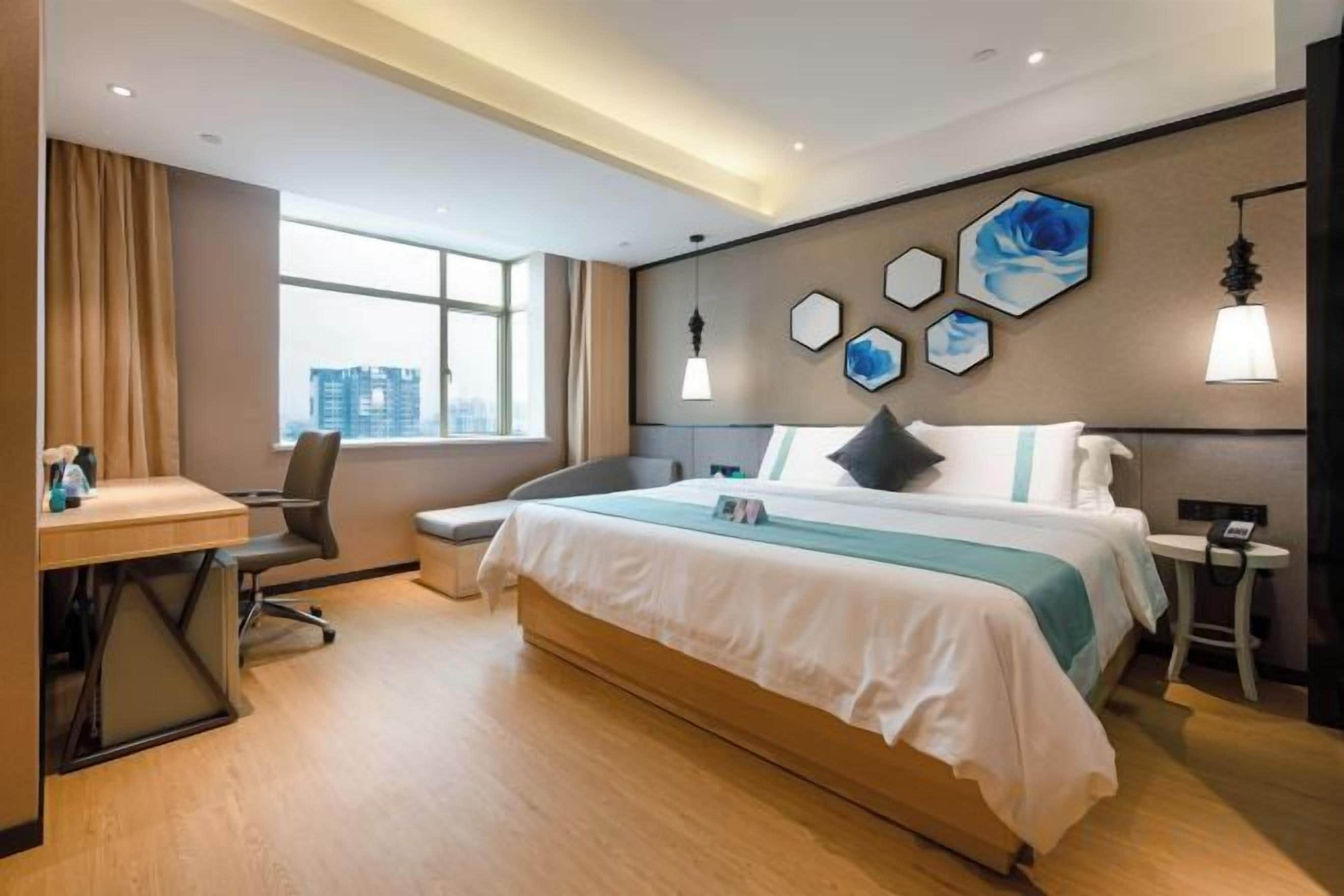 A hotel room with a bed, desk, chair, and a view of the city.