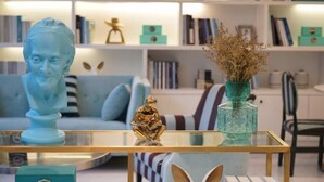 Un salon moderne avec une table basse en verre, un canapé bleu et une bibliothèque en arrière-plan.
