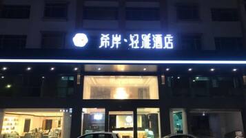 A hotel with a prominent illuminated sign, a visible entrance, and two parked cars in front.
