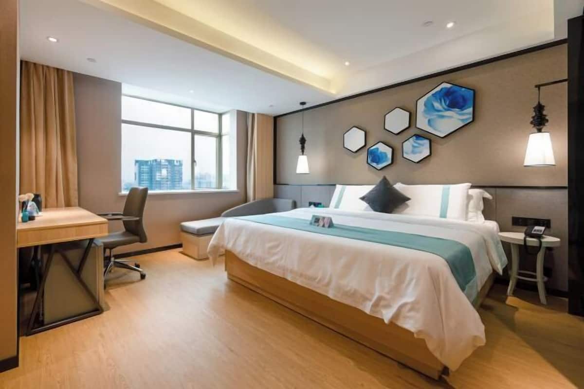 A modern hotel room with a bed, desk, and large window.