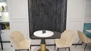 Un intérieur moderne avec une table ronde et deux chaises, un mur d’accent de couleur foncée et une bibliothèque agrémentée d’objets décoratifs.
