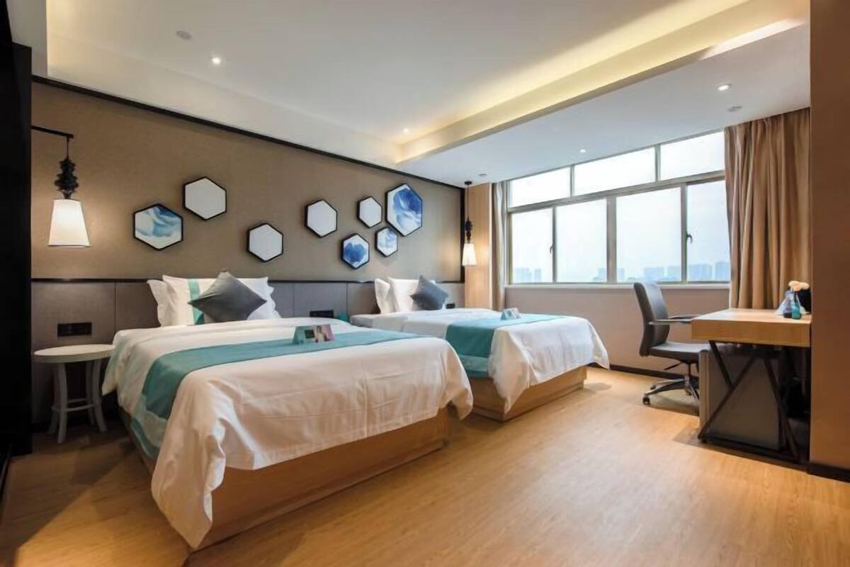 A hotel room with two beds, a desk, and a large window.