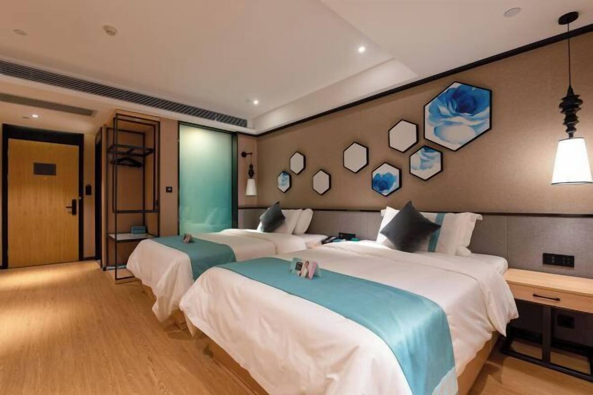 A hotel room with two beds, a wooden floor, a wardrobe, and a wall with hexagonal artwork.