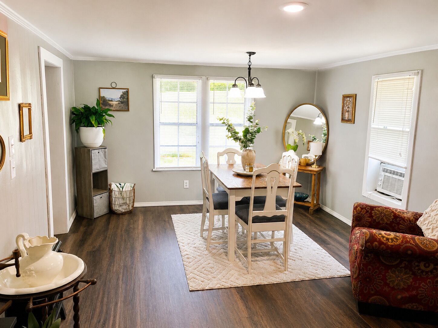 A dining area with a wooden table, chairs, a vase with flowers, and a mirror on a console table.