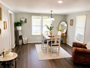 A dining area with a wooden table, chairs, a vase with flowers, and a mirror on a console table.