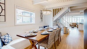 A dining area with a wooden table set for six, surrounded by wicker chairs, a chandelier, and a staircase leading to another level. - Sunshine and Bethany Beach Dreams (Bethany Beach)