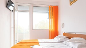 A hotel room with two beds, a large window with orange curtains, a flat-screen TV on the wall, and a view of trees outside. - HOTEL DUNAREA MAMAIA (Constanta)
