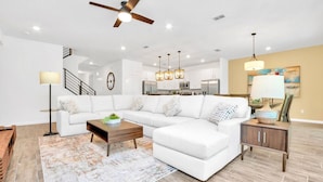 A modern living room with a sectional sofa, a coffee table, a floor lamp, and a dining area with a chandelier.