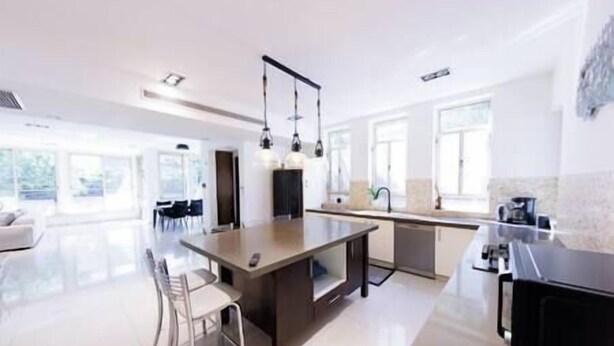 A modern kitchen with a central island, bar stools, pendant lighting, and large windows. - Five Stars Villa09 (Hod Hasharon)