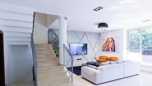 A modern living room with a staircase, a flat-screen TV, a white sofa, and a painting on the wall. - Five Stars Villa09 (Hod Hasharon)