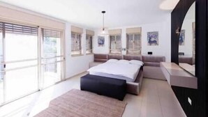A modern bedroom with a large bed, a bedside table, a mirror, and a view of the outdoors. - Five Stars Villa09 (Hod Hasharon)