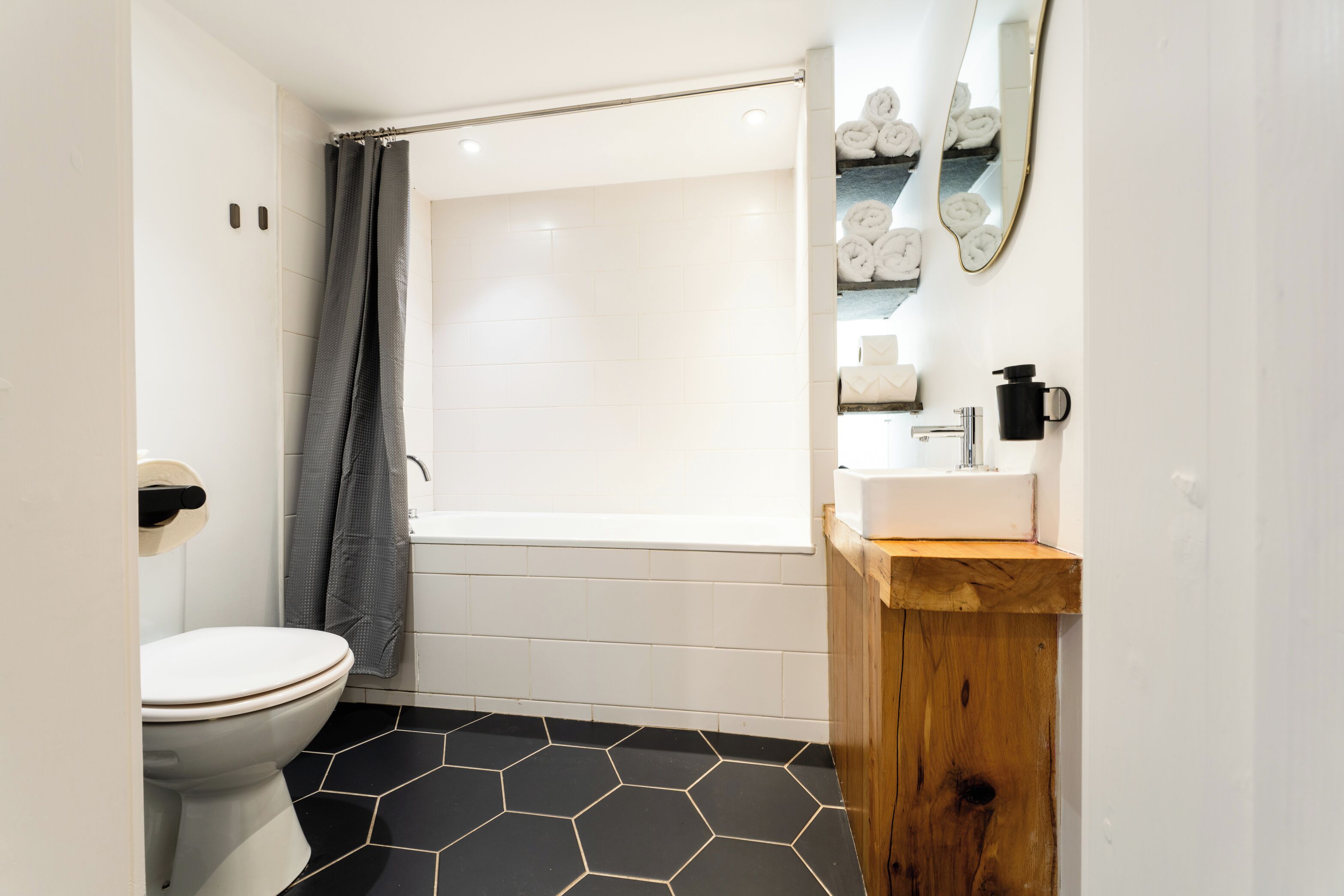Een moderne badkamer met toilet, bad, houten wastafel en spiegel.