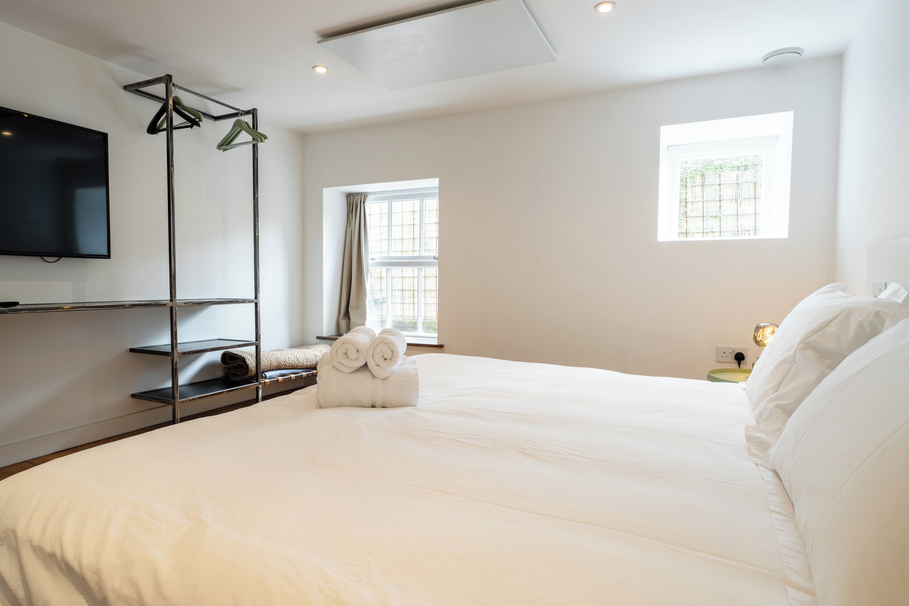 Quarto de hotel com uma cama grande, televisão de tela plana na parede e duas janelas que proporcionam luz natural.