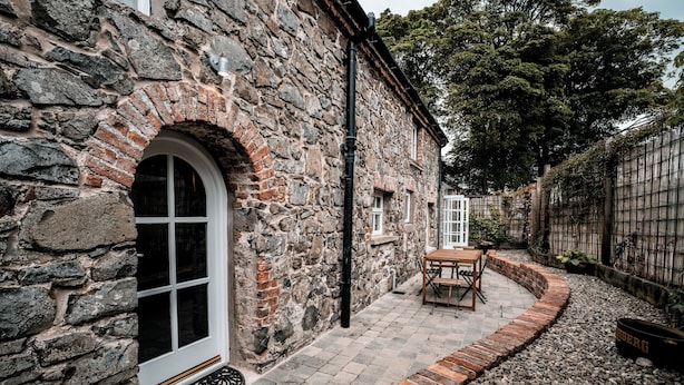A stone building with a large arched window and a small patio area with a table and chairs. - Hideout by Stay Lagom (Ballycastle)