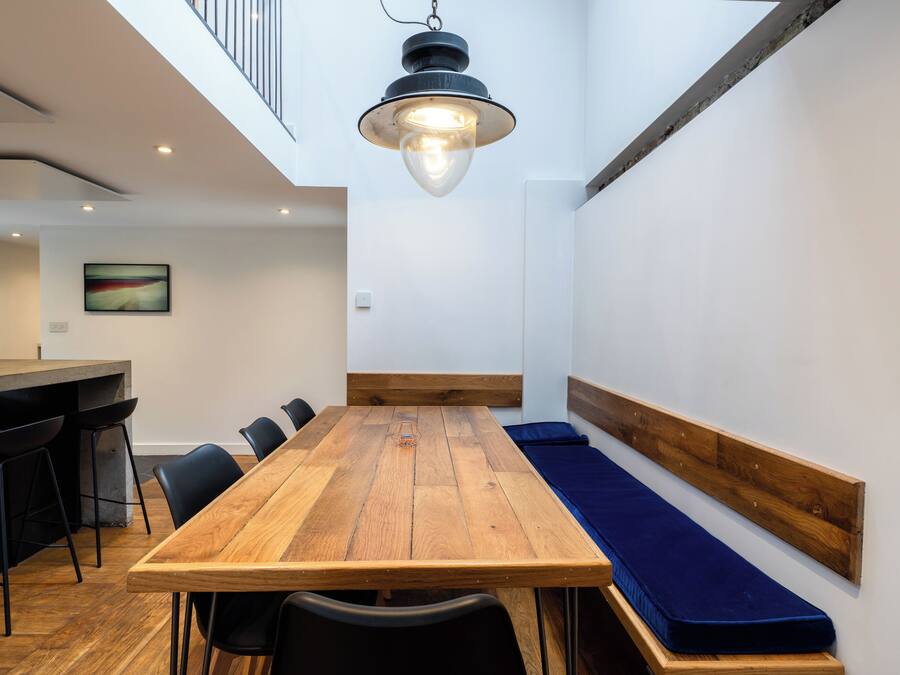 A modern interior with a wooden dining table, black chairs, a bench with a blue cushion, a hanging light fixture, and a painting on the wall.