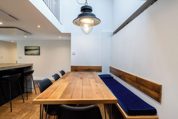 A modern interior with a wooden dining table, black chairs, a bench with a blue cushion, a hanging light fixture, and a painting on the wall.