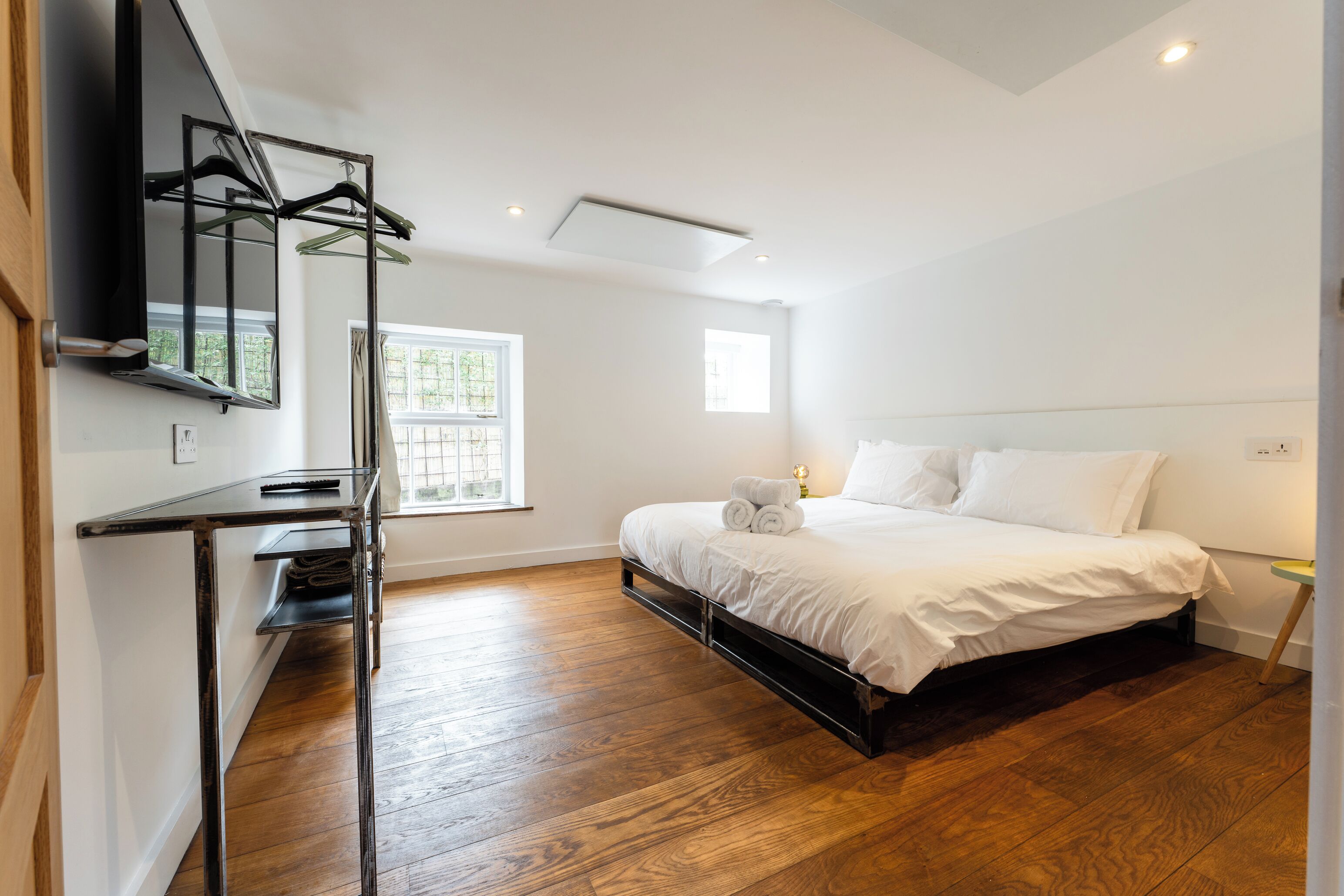 A bedroom with a bed, a desk, a TV, and a window.