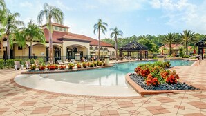 A resort pool area with a large pool, lounge chairs, palm trees, and a gazebo.