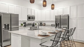 A modern kitchen with white cabinetry, stainless steel appliances, a central island with bar stools, and pendant lighting.