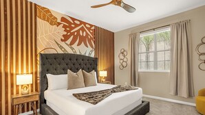 A bedroom with a tufted headboard, a large window with curtains, a wooden floor, and a ceiling fan.