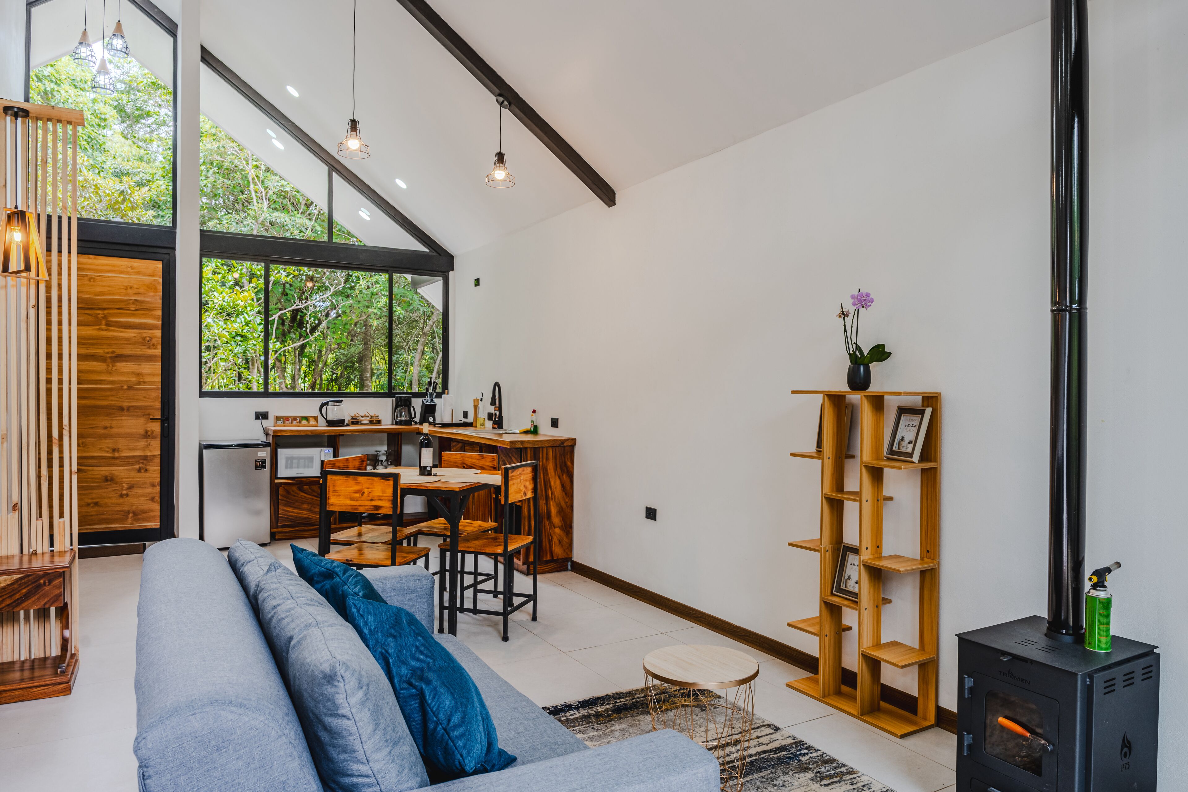 A modern living room with a sofa, a dining area, a kitchen, and a wood-burning stove.