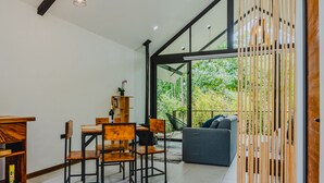 Een moderne woonkamer met een eethoek, met een grote glazen deur die leidt naar een balkon met uitzicht op groen.