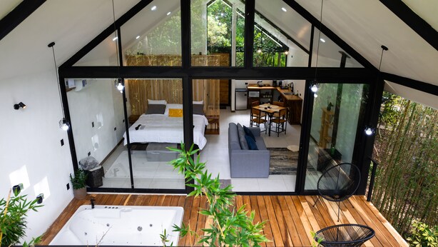 Een modern, ruim interieur met een grote glazen wand, een houten terras, een jacuzzi en een knus zitgedeelte.