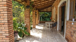 A covered patio area with a brick wall, tiled floor, and a table with chairs. - Recanto da Rose Guesthouse (Caraguatatuba)