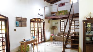A spacious living area with a high ceiling, wooden staircase, and a balcony. - Recanto da Rose Guesthouse (Caraguatatuba)