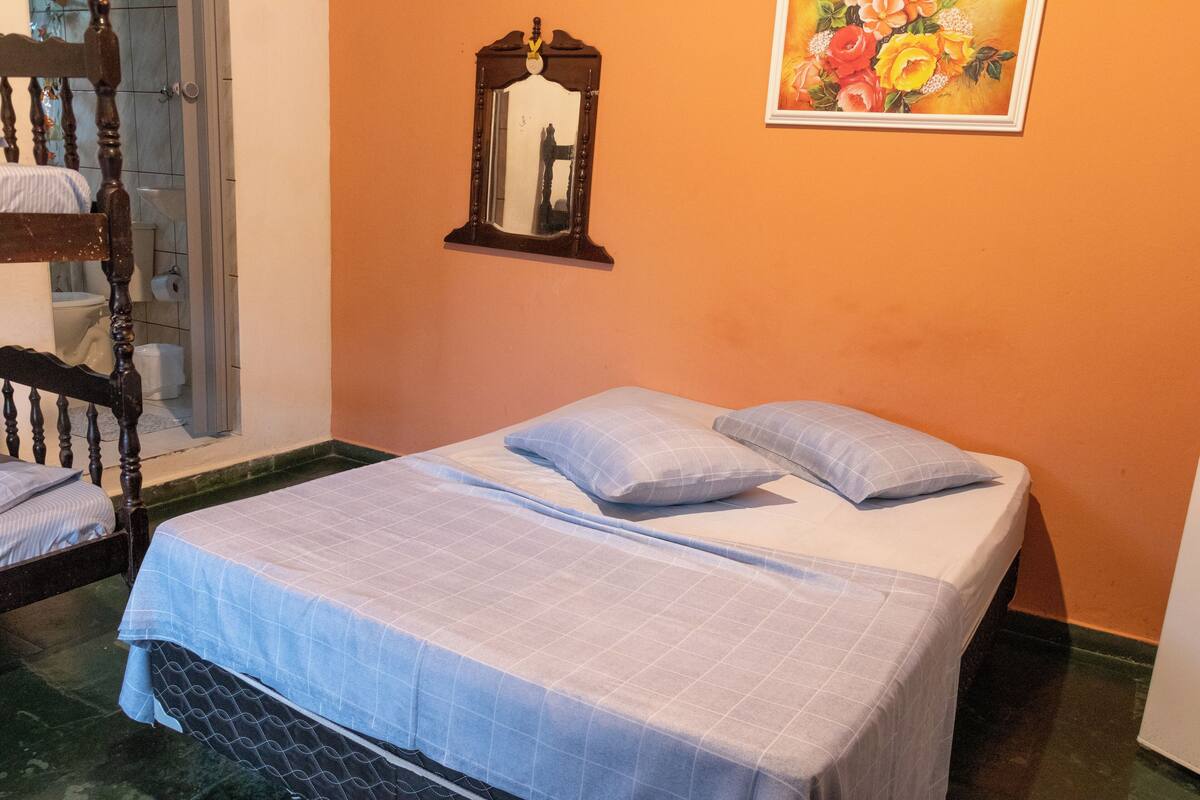 Une chambre à coucher avec un lit, des oreillers, une chaise en bois, un miroir et un tableau accroché au mur.