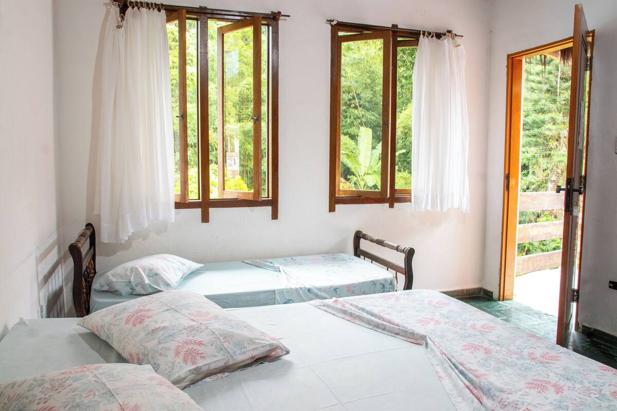 Une chambre avec deux lits simples, une tête de lit en bois et une grande fenêtre avec des rideaux.