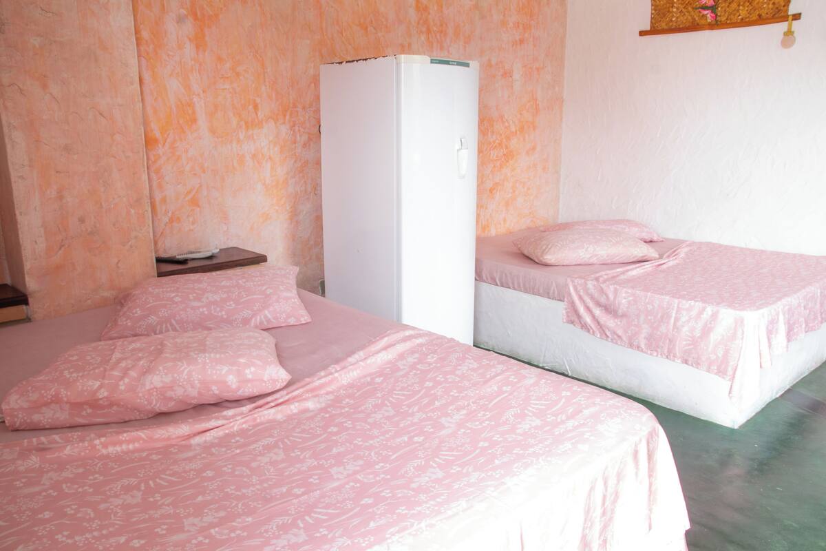 Une chambre avec deux lits, chacun agrémenté d’une literie à motifs floraux roses, d’un réfrigérateur blanc et d’une petite table en bois.