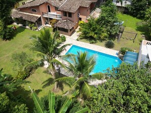 Una propietat residencial amb piscina, envoltada de vegetació abundant i palmeres.