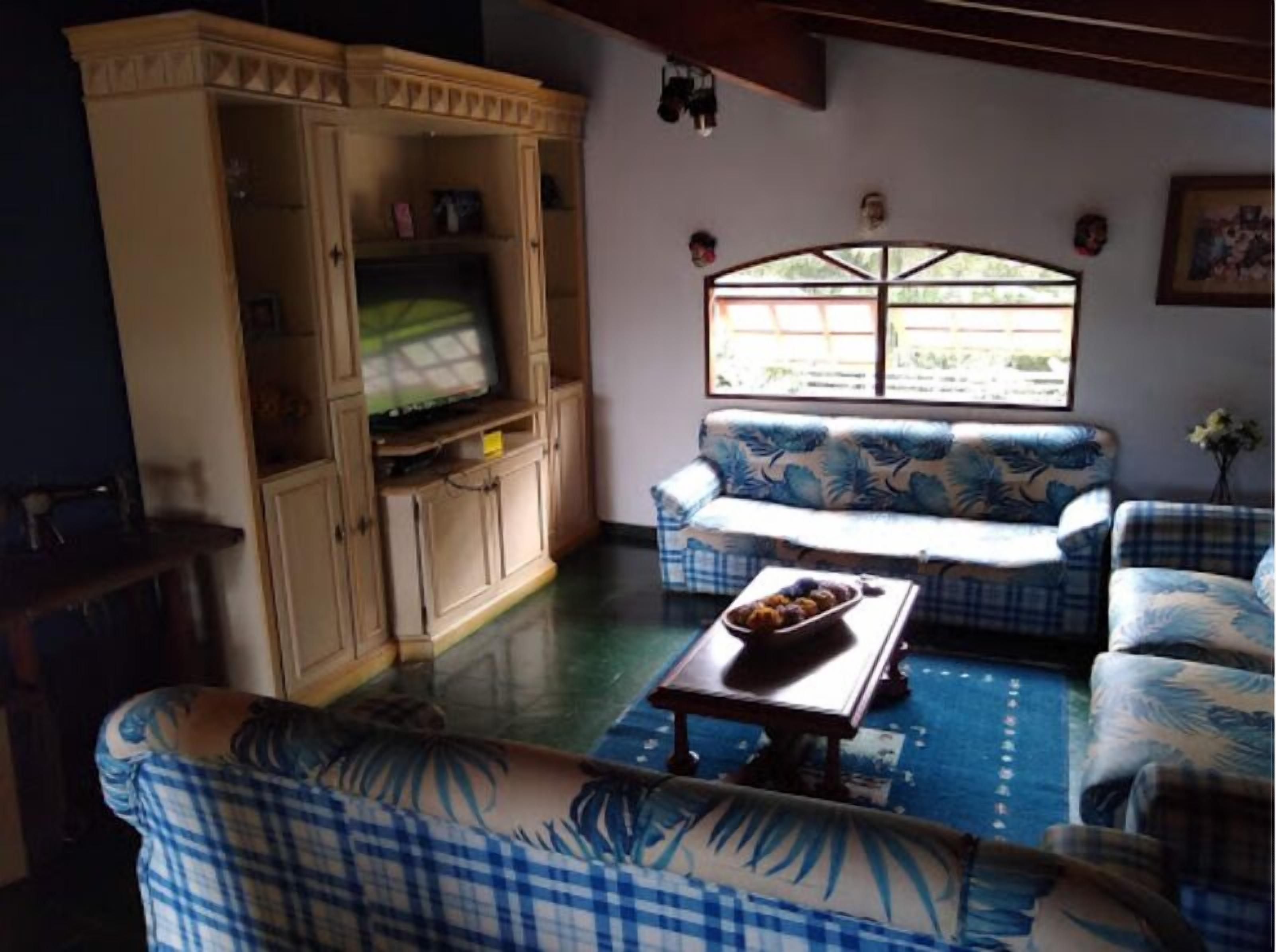 A living room with a sofa set, a television on a cabinet, and a window with a view.