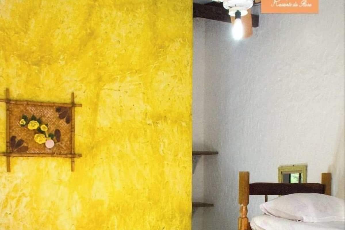 Une pièce avec un lit, des lits superposés, une petite étagère ornée de fleurs et un ventilateur de plafond.