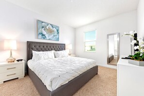 A bedroom with a large bed, a nightstand with a lamp, a dresser, and a mirror. - 20 Guest Family Mansion at Sonoma Resort (Kissimmee)